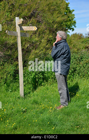L'homme de faire un choix de l'orientation du public en bois debout à côté d'un foothpath signpost (post) doigt à Snow Hill, West Wittering, West Sussex, UK Banque D'Images