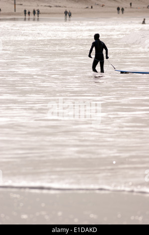 Promenades à travers l'homme tirant sa planche de surf en shore Banque D'Images