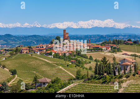 Petite ville sur la colline, entouré de vignes vertes comme des montagnes avec des sommets enneigés sur fond en Piémont, Italie du Nord. Banque D'Images