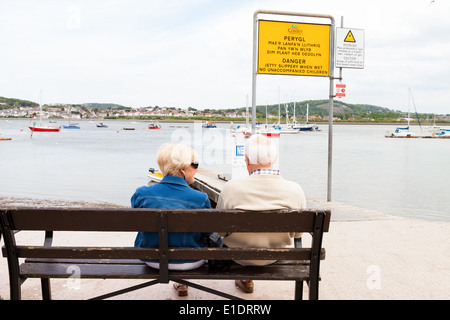 Hauts homme et femme assis sur banc en bois, profiter de la vue sur la mer, à côté de la jetée, dans le Nord du Pays de Galles Conway Banque D'Images