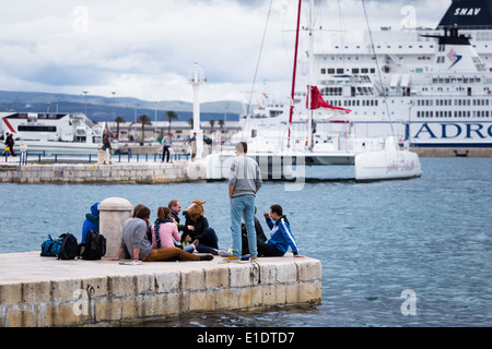 Un groupe de jeunes amis assis à split riva et bénéficiant d'une conversation avec le terminal des ferries derrière Banque D'Images