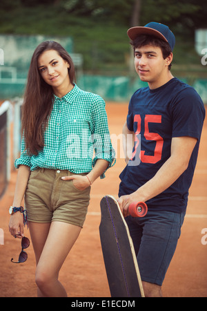 Jeune beau couple debout sur une planche à roulettes sur le court de tennis Banque D'Images