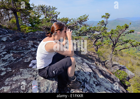 Une femme randonneur sur un rocher donnent sur l'aide de ses jumelles. Téléphone cellulaire sur sa poche. Banque D'Images