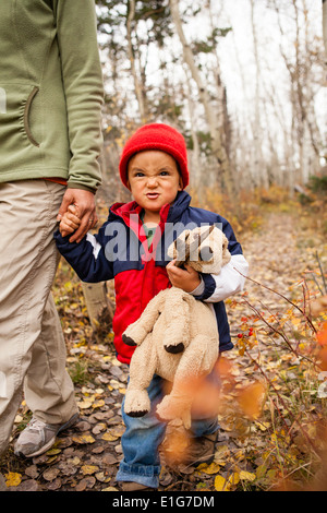 Boy holding mères main courante stuff animal sur un sentier couvert de feuilles Banque D'Images