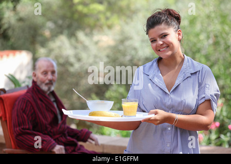 Accueil souriant carer servant repas pour le vieil homme Banque D'Images