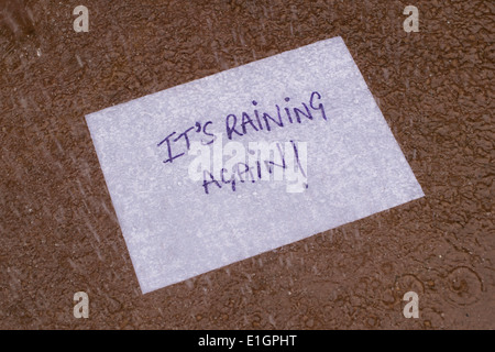 Ses à pleuvoir écrit sur un morceau de papier dans une flaque d'eau dans la pluie Banque D'Images