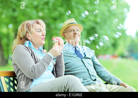 Carefree woman blowing bubbles assis sur un banc dans le parc Banque D'Images