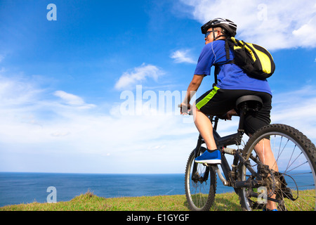 Jeune homme assis sur un vélo de montagne et à l'océan Banque D'Images