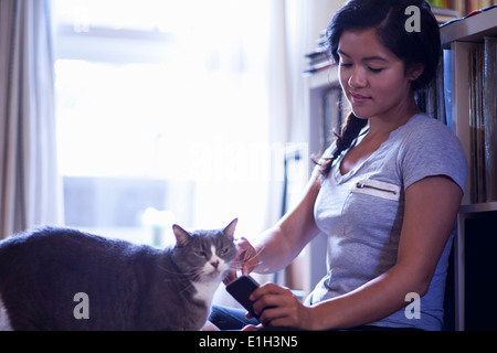 Jeune femme tenant un téléphone cellulaire stroking cat Banque D'Images
