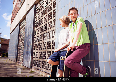 Boys leaning against wall with skateboards Banque D'Images