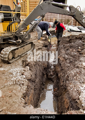 L bâtiment maison, les hommes l'excavation des fossés pour les drains avec mini machine digger excavator Banque D'Images