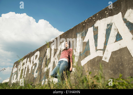 Young woman leaning against wall avec graffiti Banque D'Images