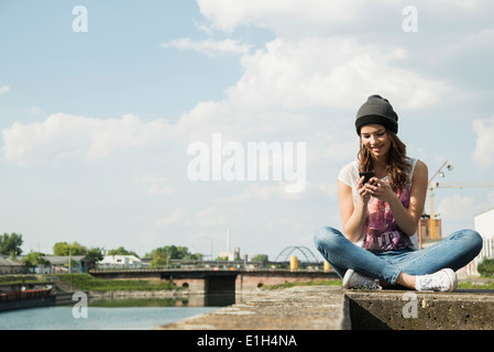 Young woman sitting on wall using cell phone Banque D'Images