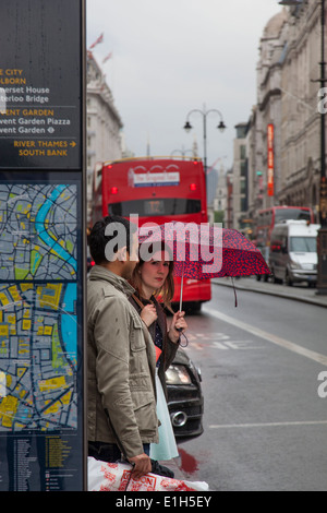 Femme tenant un parapluie s'apprête à traverser le Strand à Londres avec un bus à impériale rouge toit à l'arrière-plan. Banque D'Images