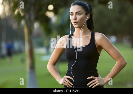 Mid adult woman wearing earphones, mains sur les hanches Banque D'Images