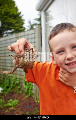 Portrait of young boy in garden holding up toad Banque D'Images