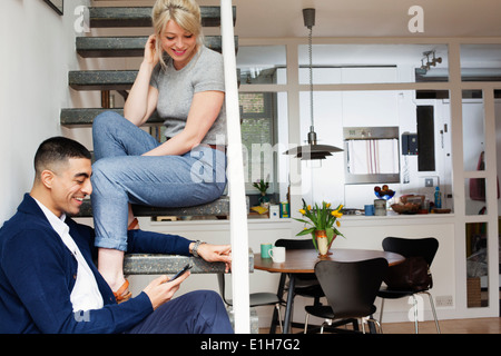 Jeune homme et femme assis sur les escaliers, looking at smartphone Banque D'Images