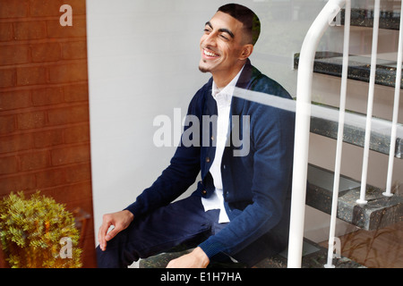 Jeune homme assis sur les escaliers, smiling Banque D'Images