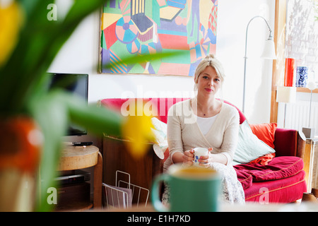 Young woman relaxing in living room avec tasse de thé Banque D'Images