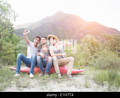 Trois jeunes hommes assis sur le dessus de canoe, taking self portrait photograph Banque D'Images