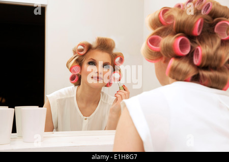 Young woman in curlers mise sur make-up Banque D'Images