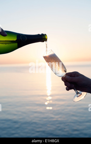 Le champagne est versé dans la flûte contre coucher du soleil Banque D'Images