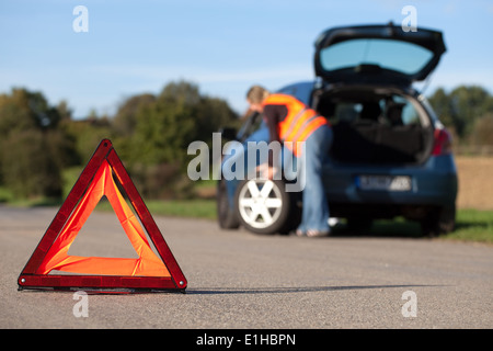 Changement de pneu sur une voiture en panne avec un triangle d'avertissement rouge Banque D'Images