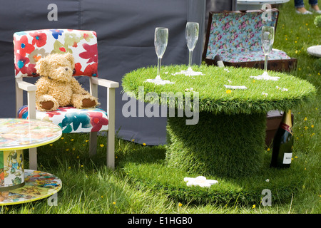 Ours assis sur une chaise à côté d'une table Astroturf et verres à vin Banque D'Images