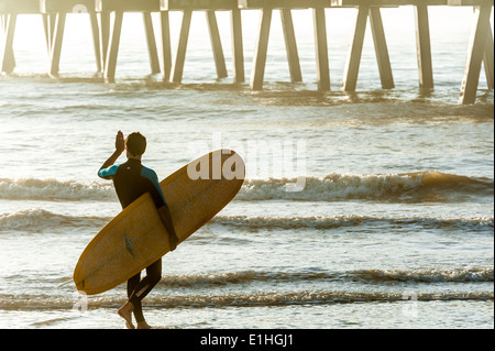 Un surfeur Floride protège les yeux contre l'éblouissement du soleil levant comme il entre dans l'eau à Jacksonville Beach. USA. Banque D'Images