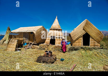 Femme de l'Uros indiens en face de huttes de roseaux typique et traditionnel four en argile à l'avant-plan, les îles flottantes faites de roseaux Banque D'Images