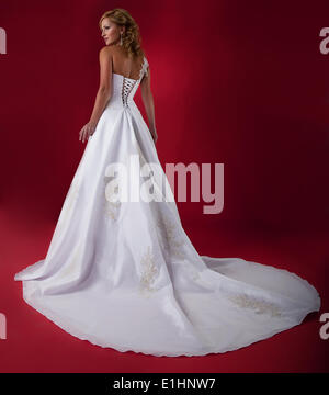 Blonde à la mode jeune épouse en robe de mariage blanc sur fond rouge. Studio shot Banque D'Images