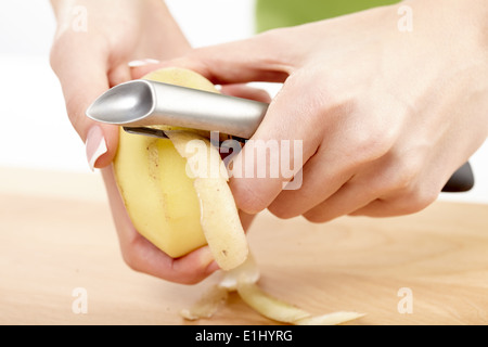 Mains d'une jeune femme avec peler ustensile de cuisine sur une planche en bois Banque D'Images