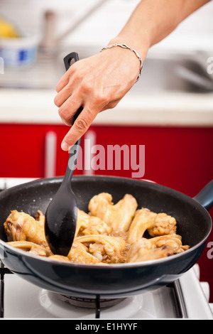 La main de femme dans un wok en remuant les ailes de poulet après une recette asiatique Banque D'Images