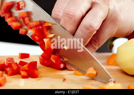 Les mains d'un homme hacher les légumes sur une planche en bois Banque D'Images