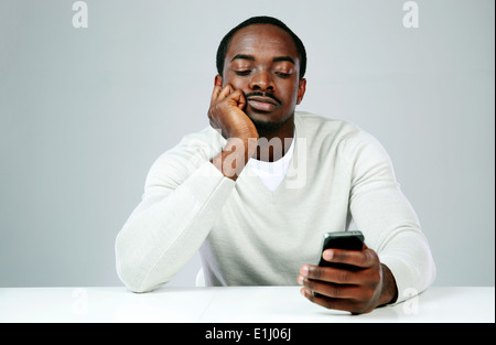 Pensive african man using smartphone sur fond gris Banque D'Images