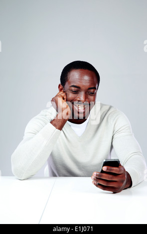 Afrique joyeuse l'homme assis à la table et using smartphone Banque D'Images
