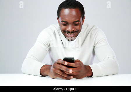 L'Afrique de l'Heureux l'homme assis à la table et using smartphone Banque D'Images