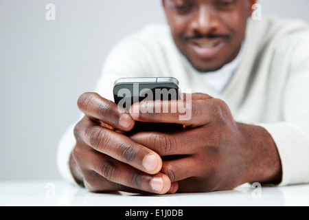African l'homme assis à la table et l'utilisation de smartphone. L'accent sur le smartphone. Banque D'Images