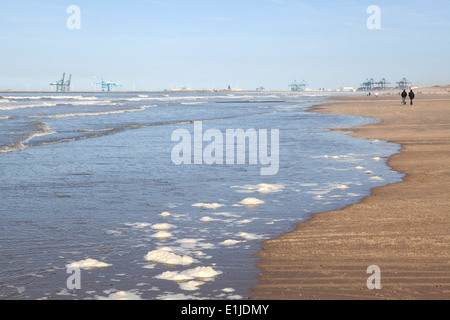 Vue éloignée sur couple strolling on beach avec grues portuaires sur l'horizon, Ostende, Belgique Banque D'Images