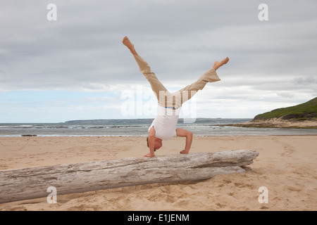 Young man doing handstand on tree trunk at beach Banque D'Images