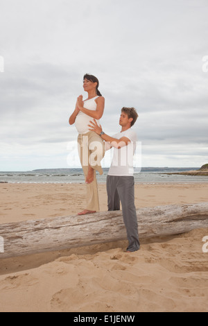 Pregnant woman practicing yoga avec entraîneur personnel at beach Banque D'Images