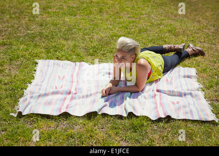 Jeune femme couchée sur un tapis sur l'herbe du parc Banque D'Images