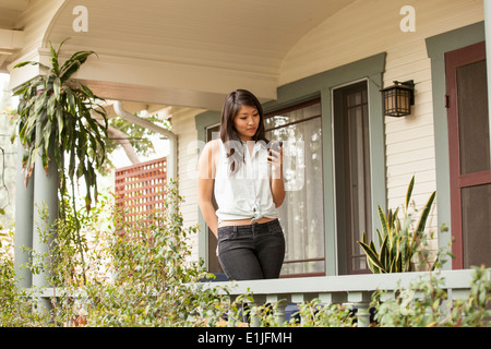 Young woman using smart phone on porch Banque D'Images