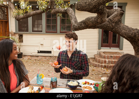 Amis assis autour de la table barbecue partage la nourriture, man juggling fruit Banque D'Images