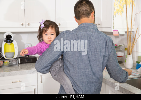 Mid adult man carrying toddler daughter in kitchen Banque D'Images