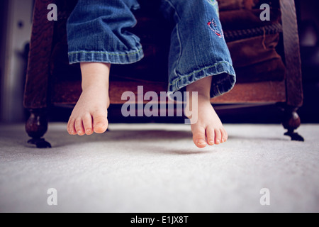 Les petits pieds et les jambes pendantes sur une chaise Banque D'Images