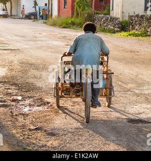 Retour à la maison après le travail. Un vendeur de vélos chaussés de tongs, esquives de poule sur une rue de Tulum. Banque D'Images