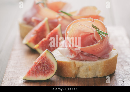 Des canapés avec jambon et figues sur table, aux tons vintage Banque D'Images