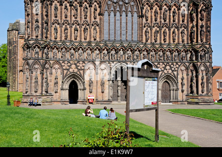 Façade ouest de la cathédrale avec groupe de gens assis sur la pelouse à l'avant-plan, Lichfield, Angleterre, Royaume-Uni, Europe de l'Ouest. Banque D'Images