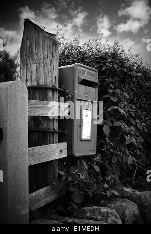 Petit royal mail post box en bois fixée à un grand poster en milieu rural. Image en noir et blanc avec ciel dramatique Banque D'Images